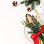 Traditional Christmas table place setting. Golden cutlery, linen napkin, spruce branches and cup of milk. Pine cone and red ribbon decoration. Holidays background. Flat lay, top view with copy space.